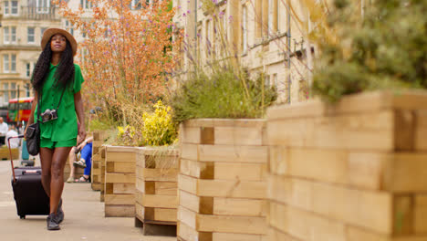 Turista-Femenina-Con-Cámara-De-Vacaciones-En-Oxford,-Reino-Unido,-Explorando-La-Ciudad-Caminando-Por-Una-Calle-Ancha-Tirando-De-Una-Maleta-Con-Ruedas